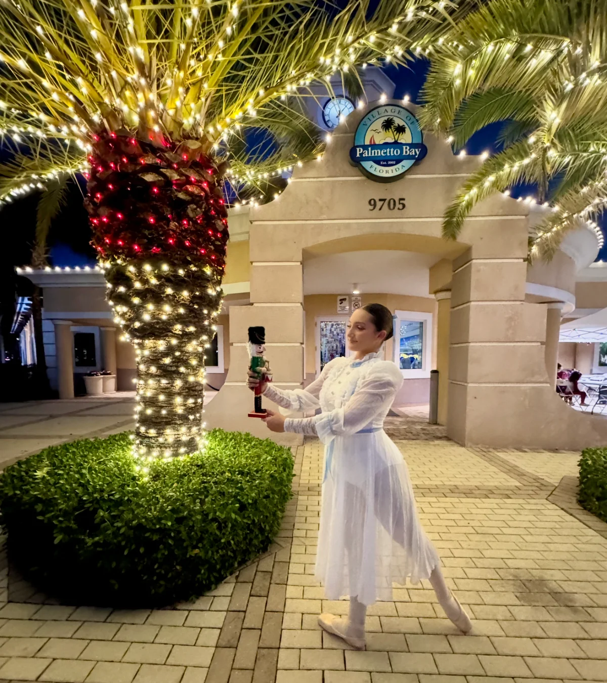 Ballet at the Park dancer holding a nutcracker outside the lit-up Palmetto Bay Village Hall